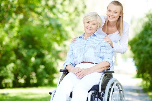 Female caregiver and senior patient in a wheelchair looking at camera outside